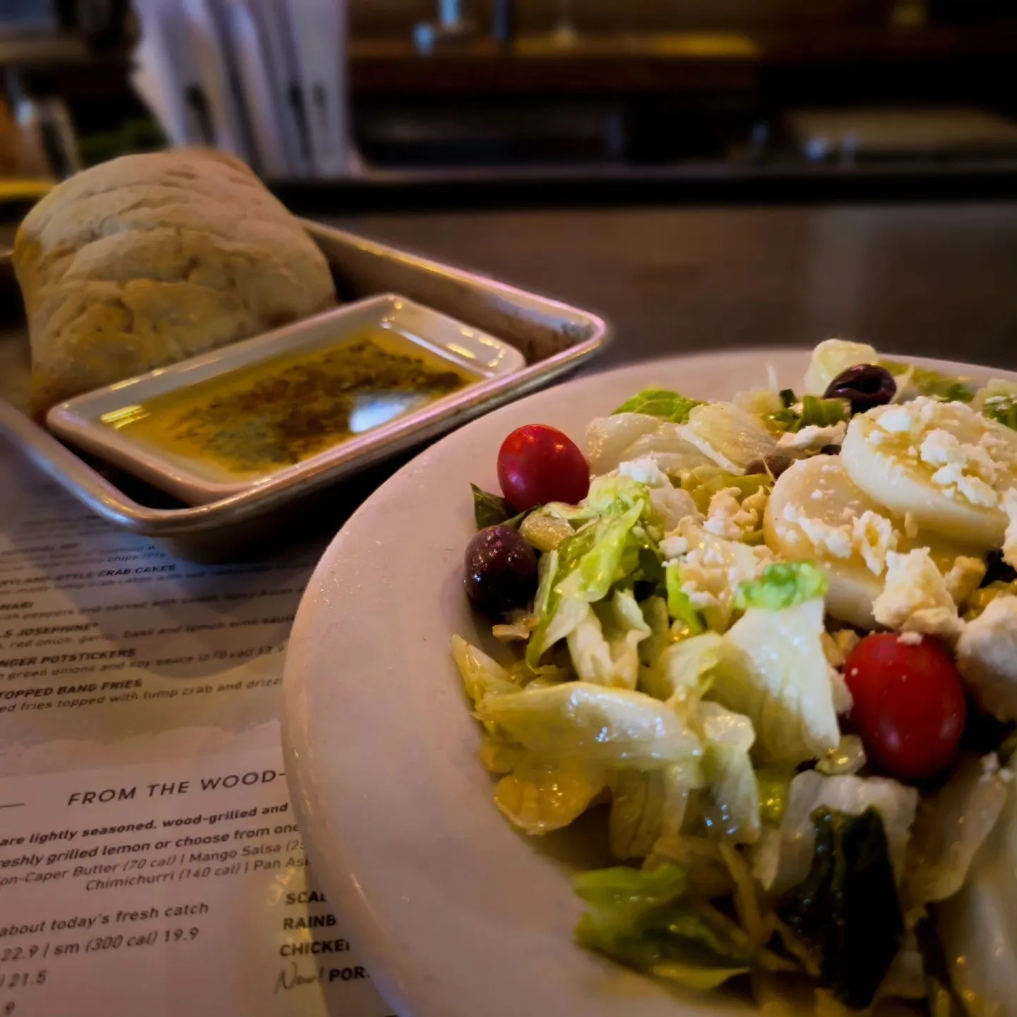 A salad with tomatoes, olives and sliced egg beside bread and a dish of dipping oil.