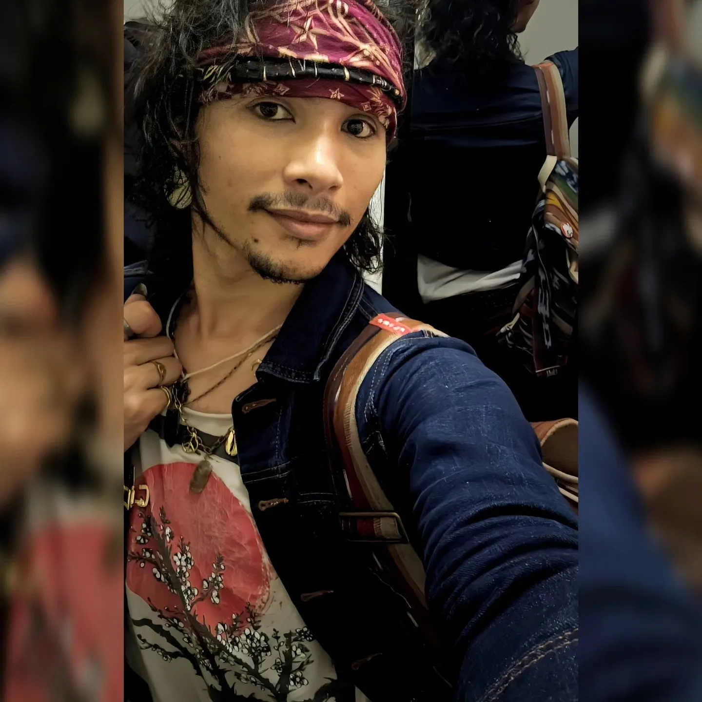 A portrait of a person wearing a patterned headband, necklaces and a dark jacket.