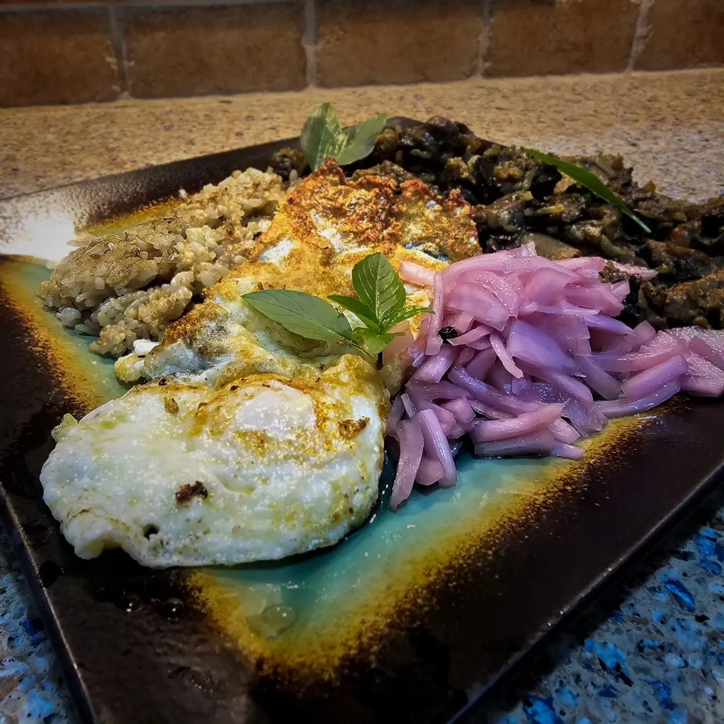 A breakfast plate with eggs, grains, browned mushrooms and pink pickled onions.