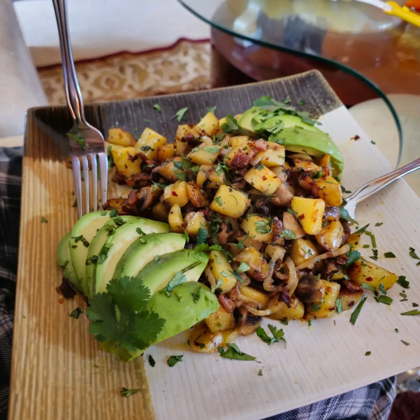 A plate of browned potatoes and vegetables with sliced avocado and fresh herbs.