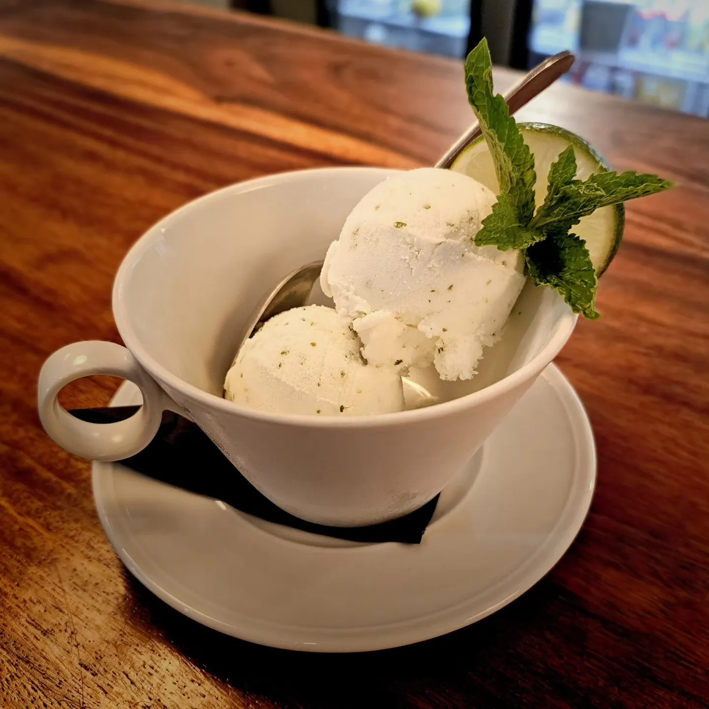 Two scoops of pale ice cream in a teacup, garnished with a lime slice and mint.