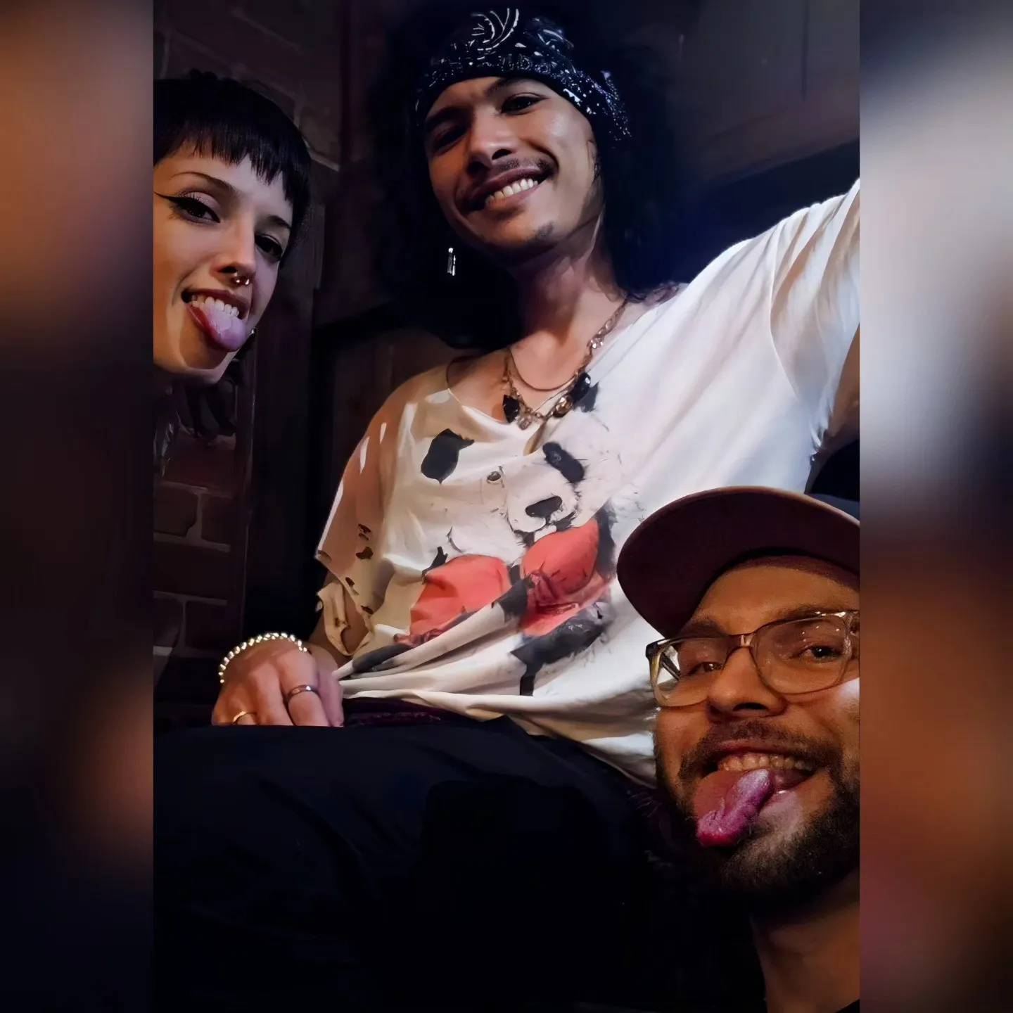 Three smiling people lean into a group portrait indoors.
