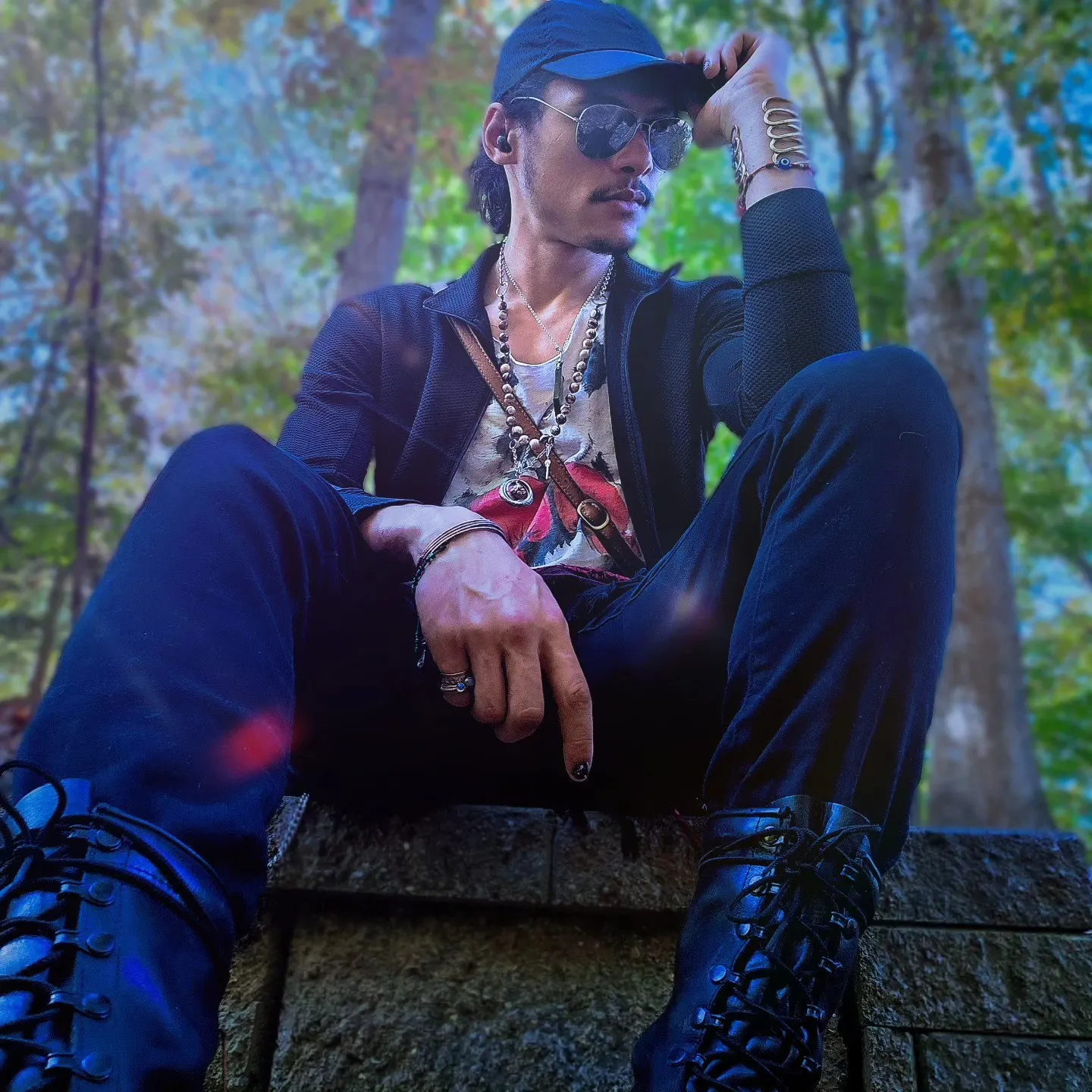 A person in a black cap and dark clothes sits on stone steps among trees.