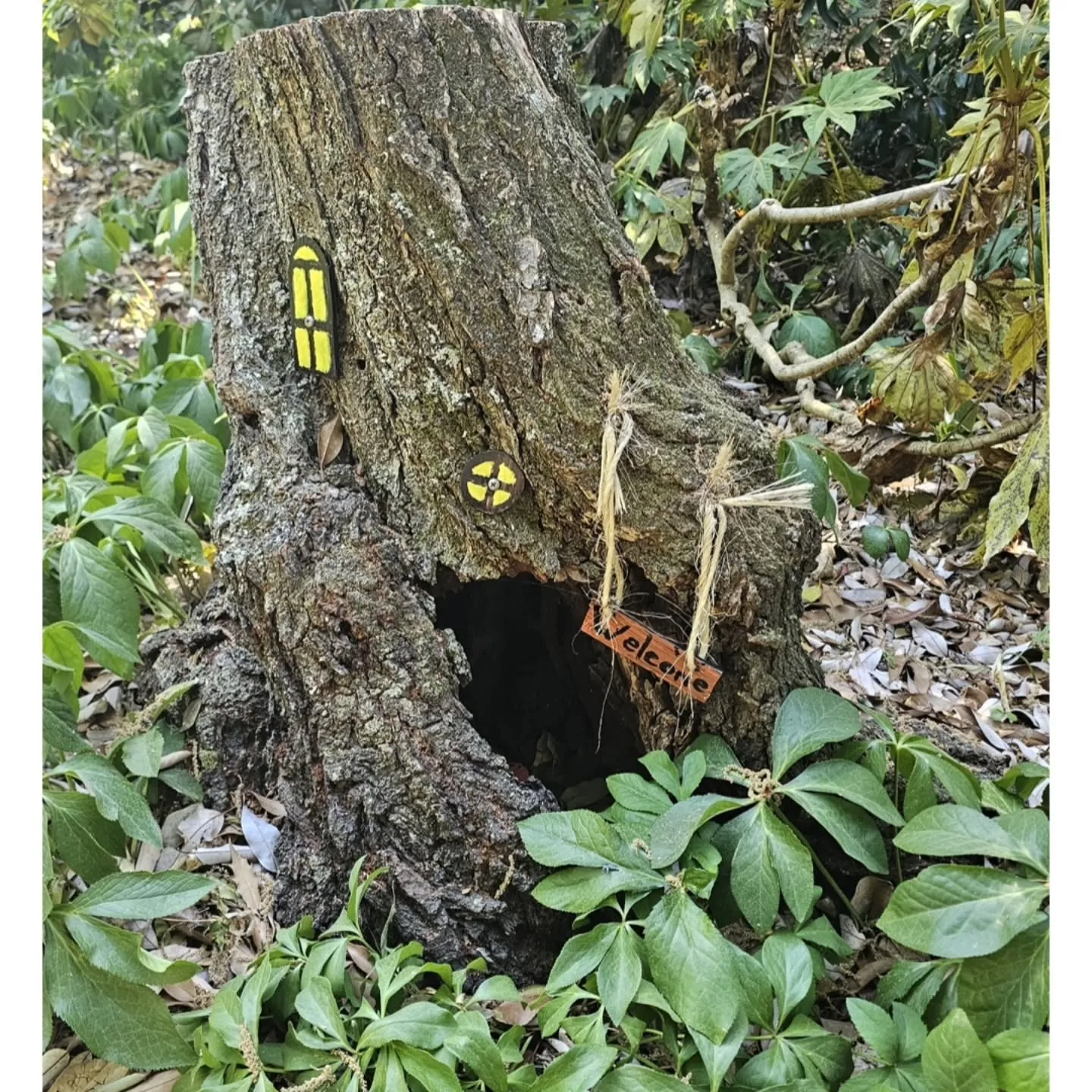 Tiny decorative windows and a miniature bridge turn a hollow tree trunk into a fairy house.