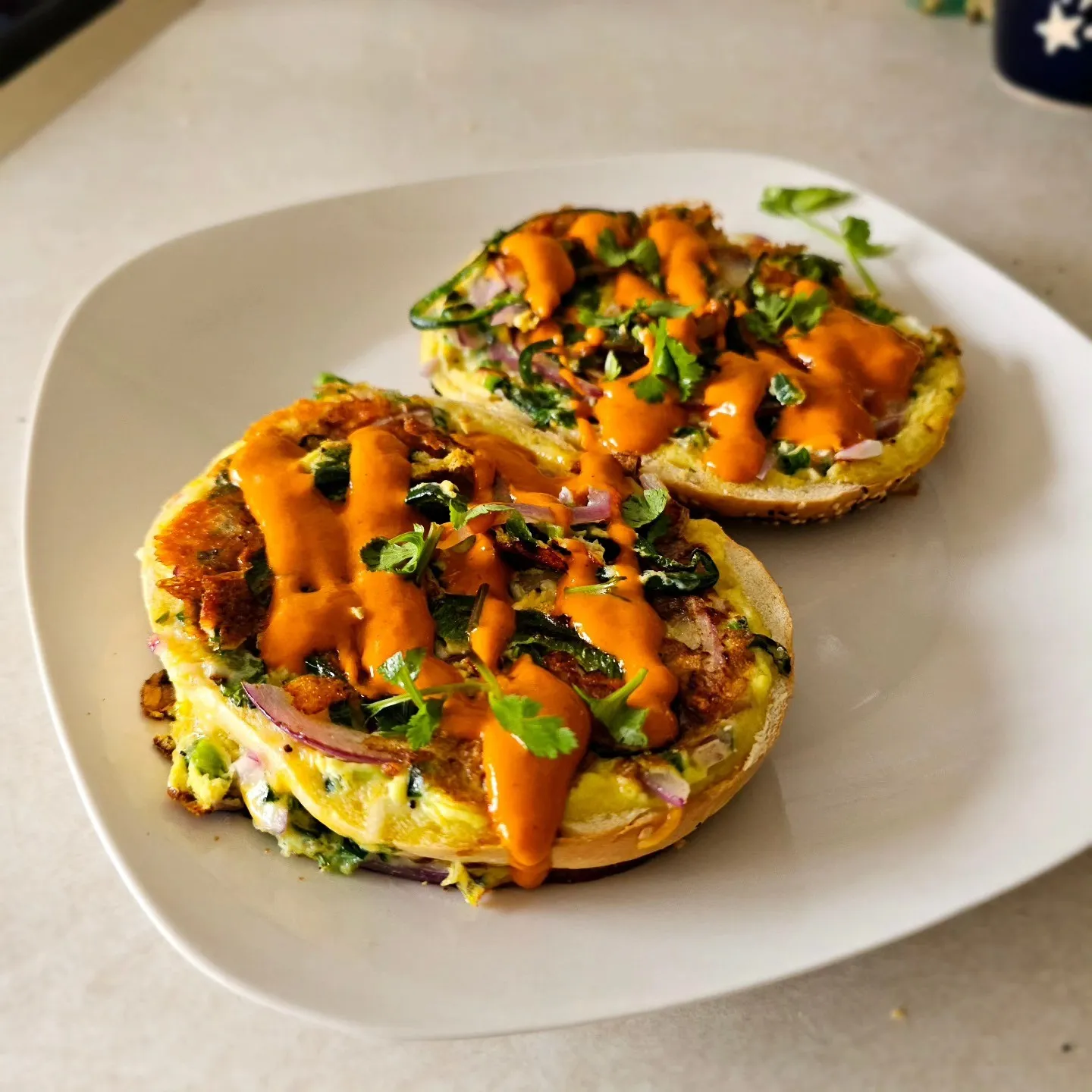 Two open-faced sandwiches topped with greens, sliced vegetables and orange sauce.