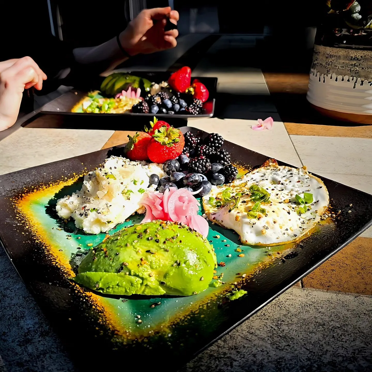 A colorful breakfast plate with eggs, avocado, berries and pink pickled onions.