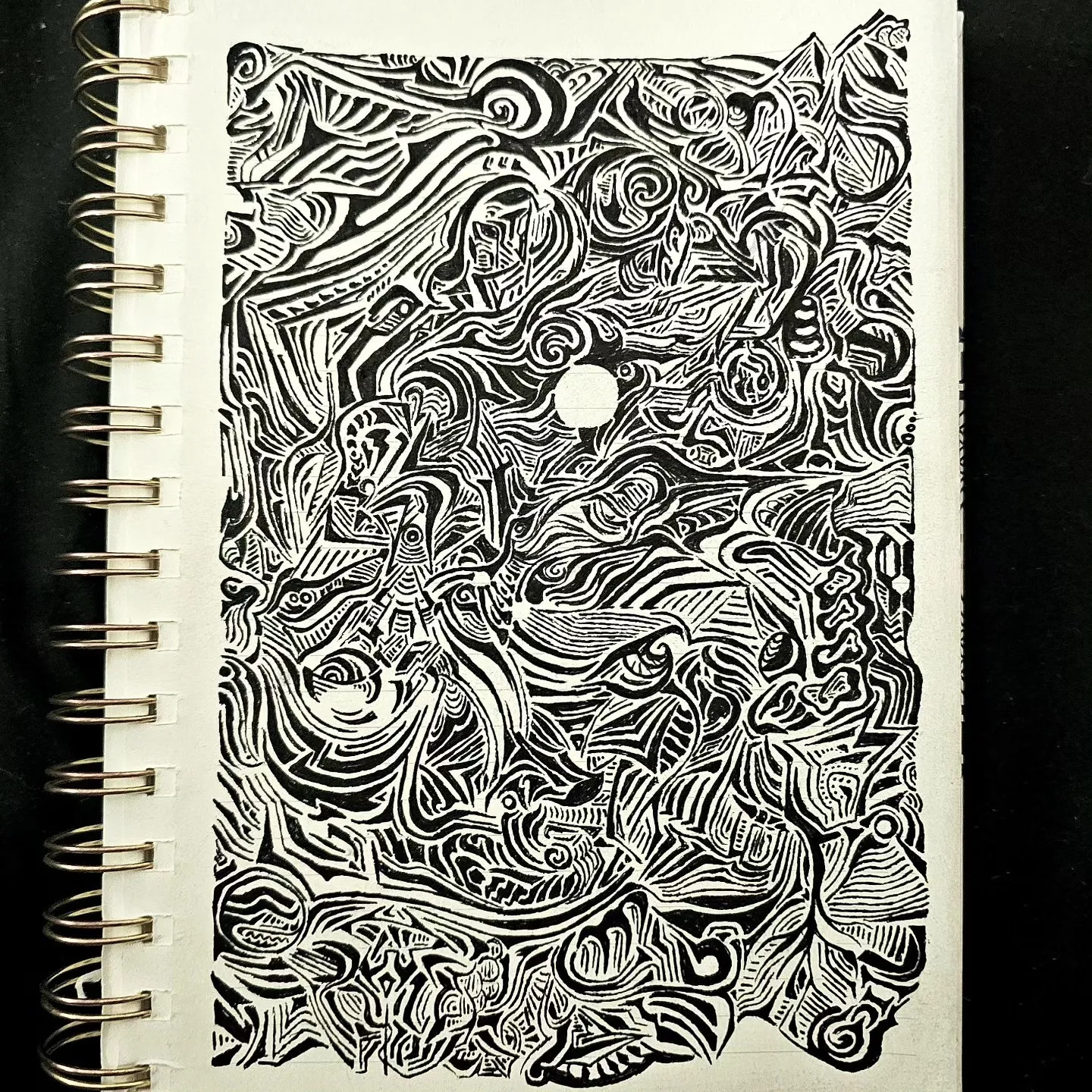 A sketchbook page filled with intricate black ink lines, swirling shapes and small faces.