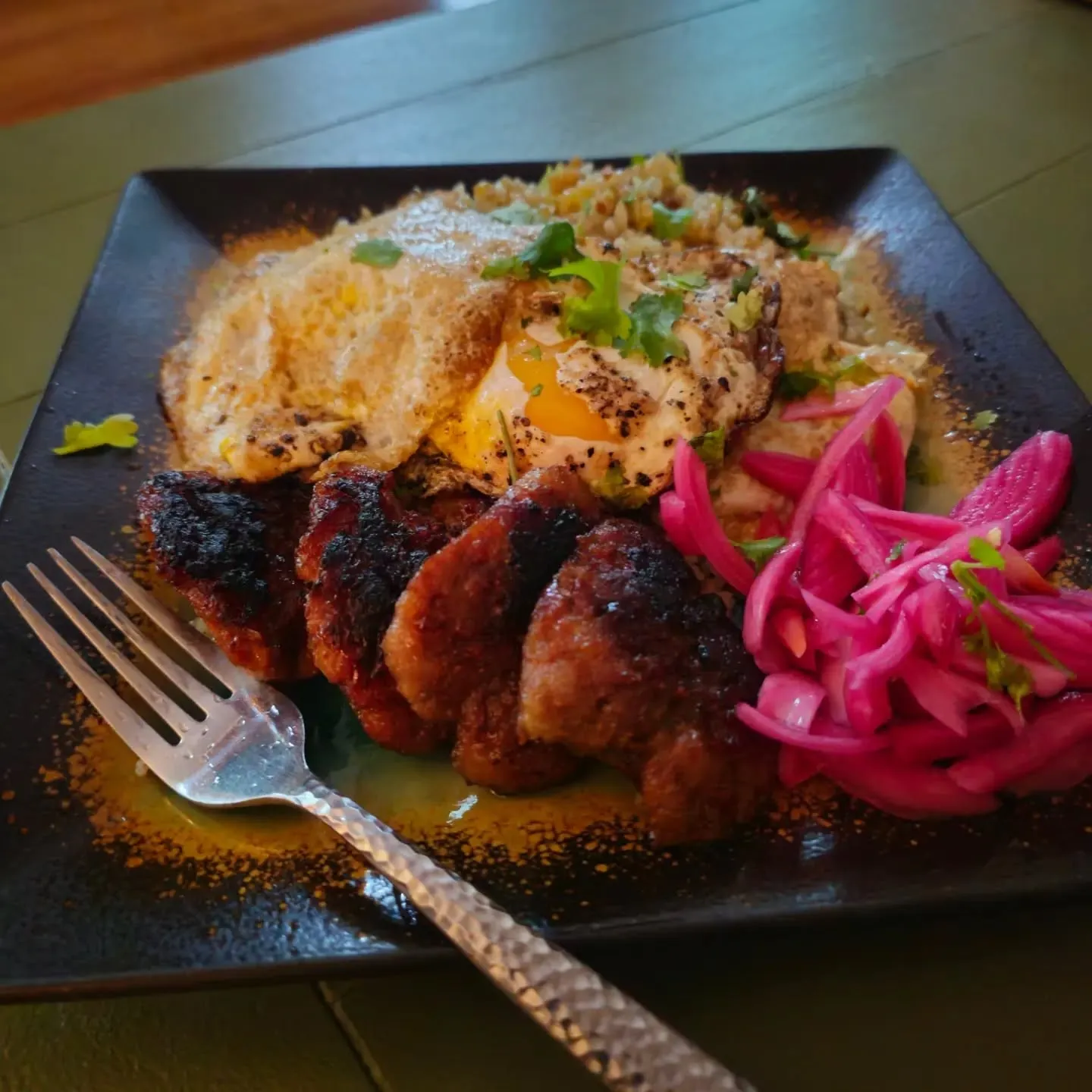 A breakfast plate with browned patties, eggs, grains and bright pink pickled onions.