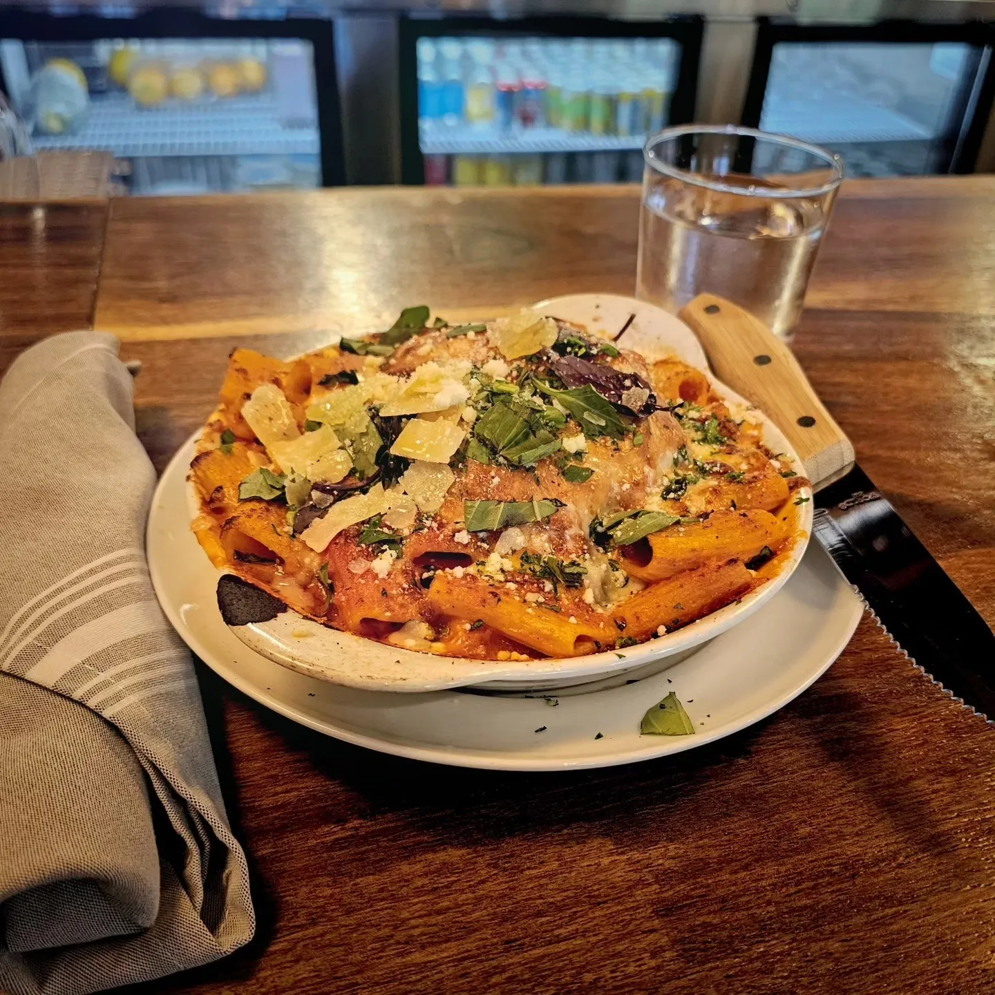 A bowl of pasta in red sauce, topped with cheese shavings and herbs, sits on a bar.