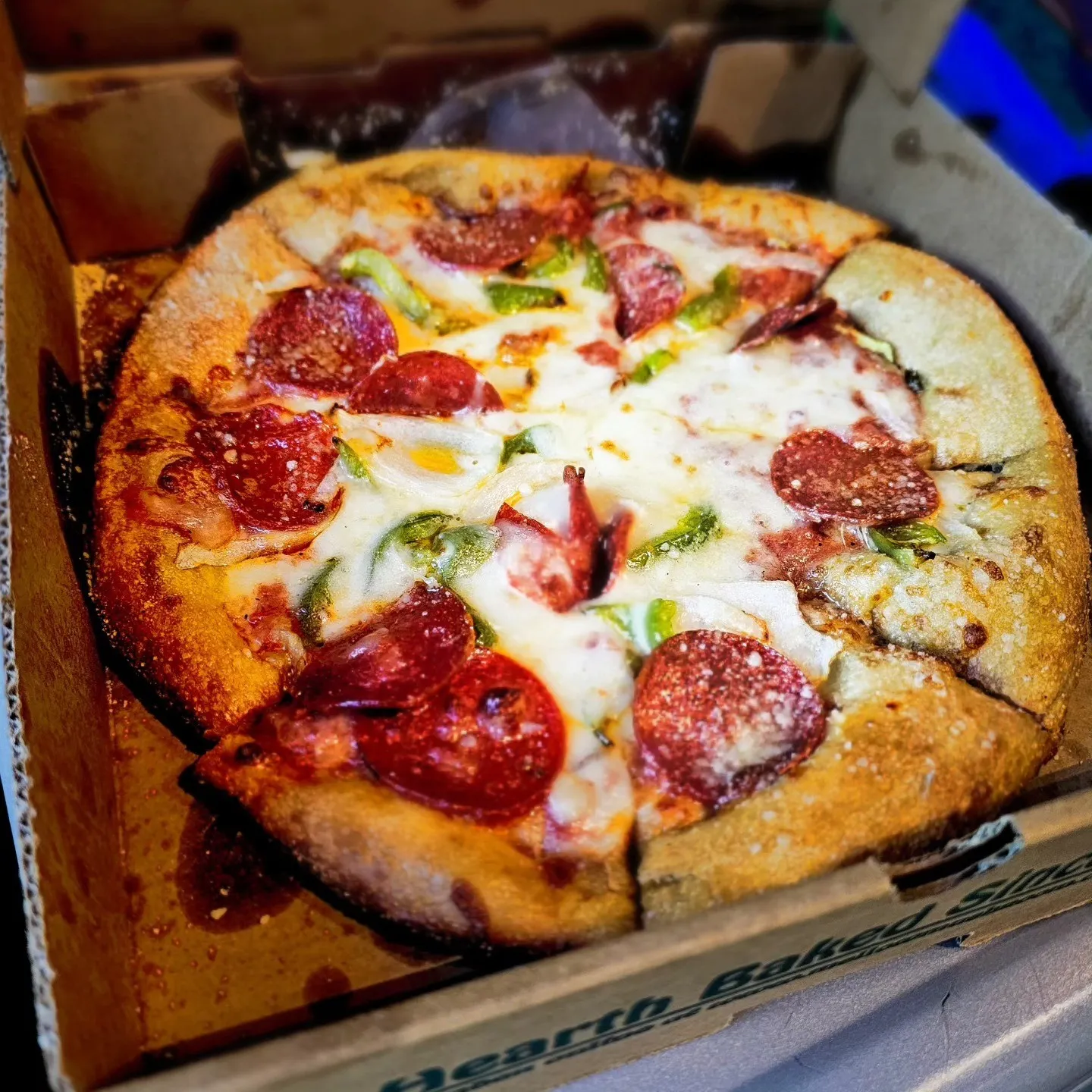A thick-crust pizza topped with melted cheese, pepperoni and green peppers in its box.