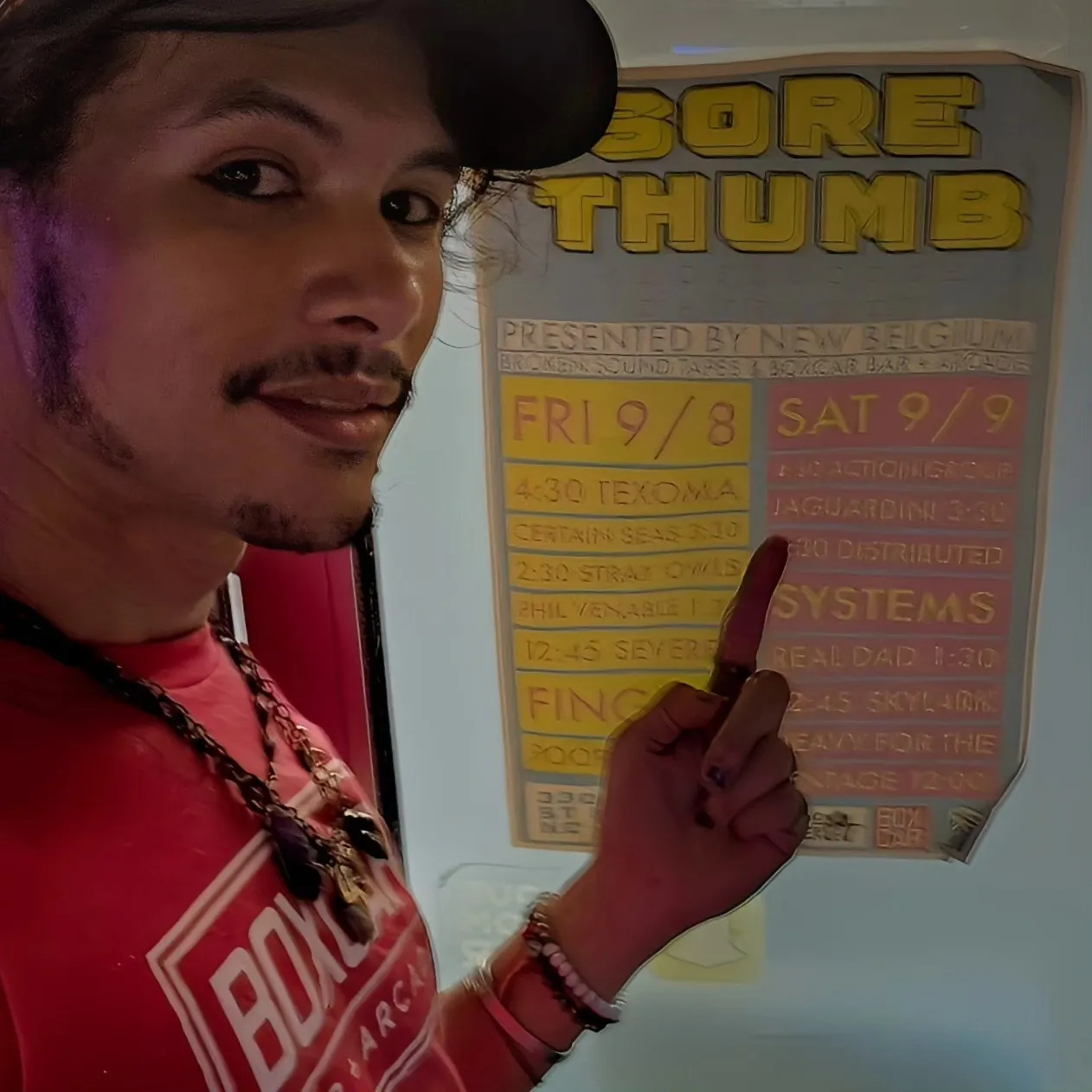 A person points to a Sore Thumb event poster while taking a selfie.