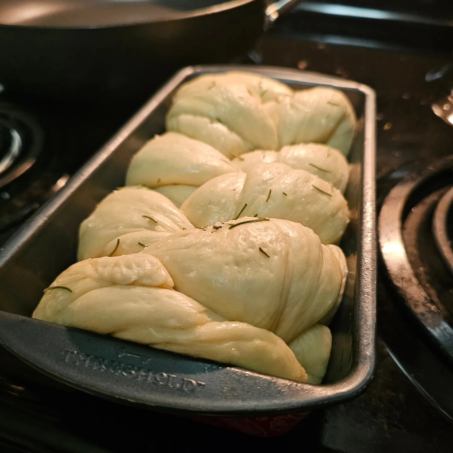 A braided loaf of pale dough rests in a rectangular baking tin.