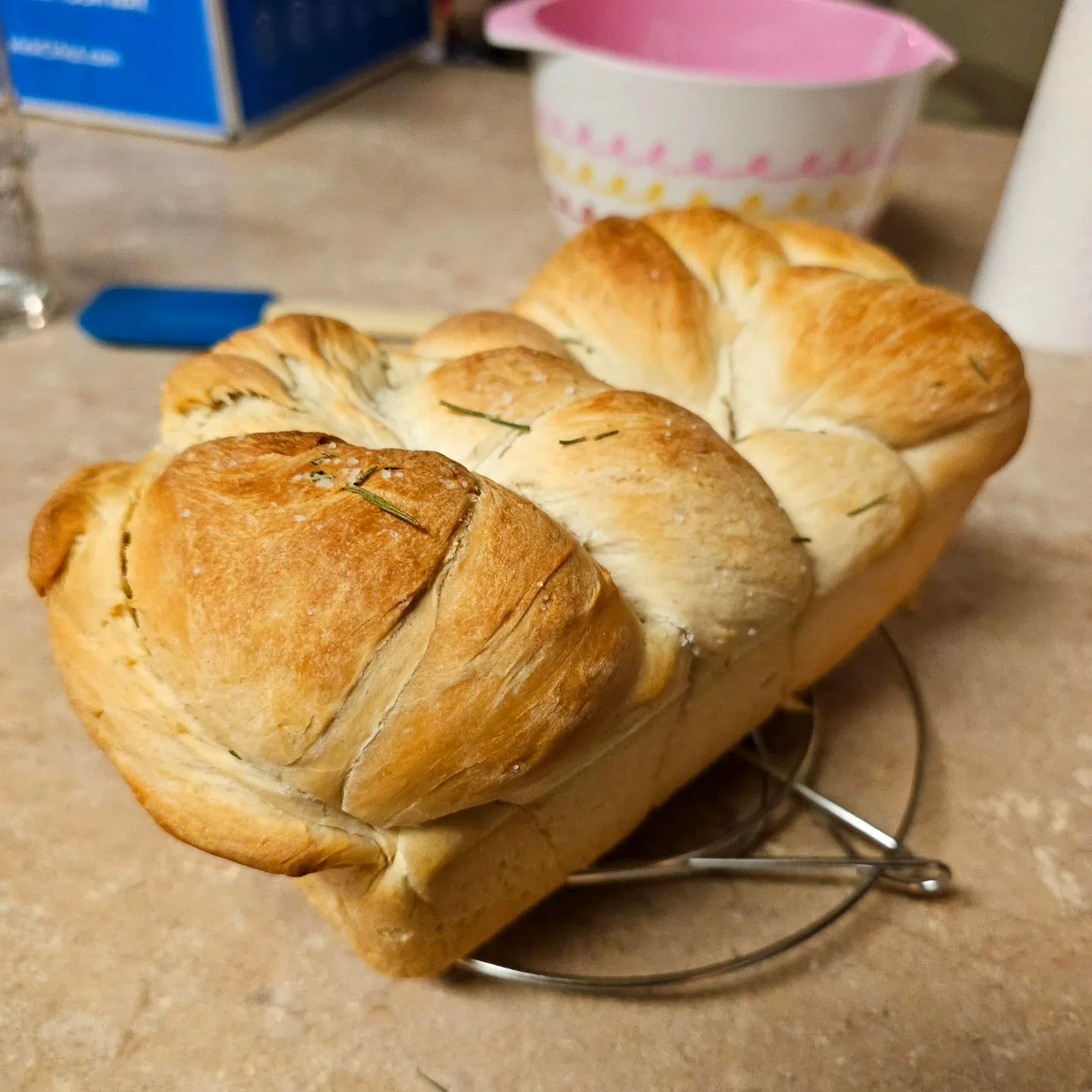 A golden braided loaf cools on a small rack on a kitchen counter.