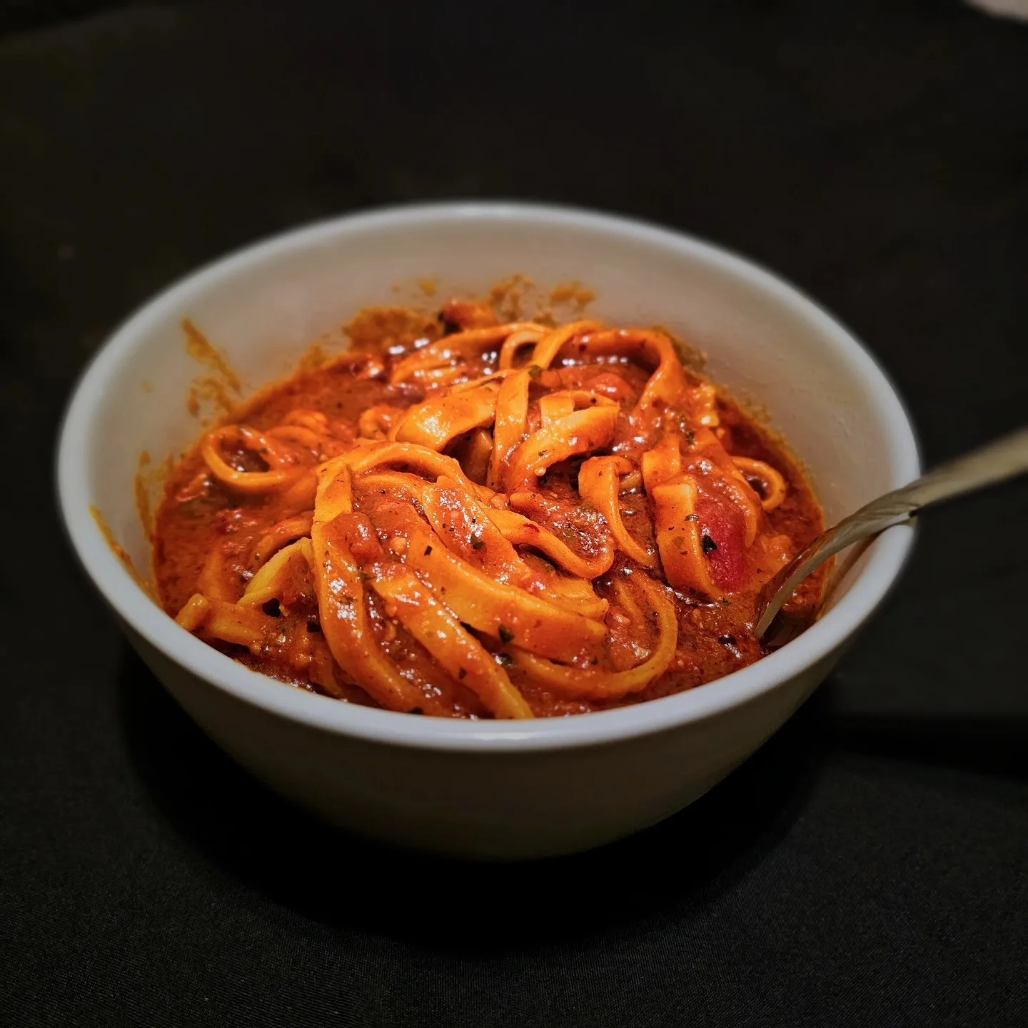 A bowl of ribbon-shaped pasta coated in red sauce with a fork resting inside.