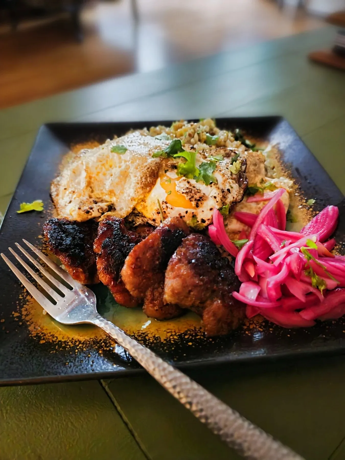 Longanisa and a fried egg over garlic fried rice, with bright pink pickled onions on a black plate.