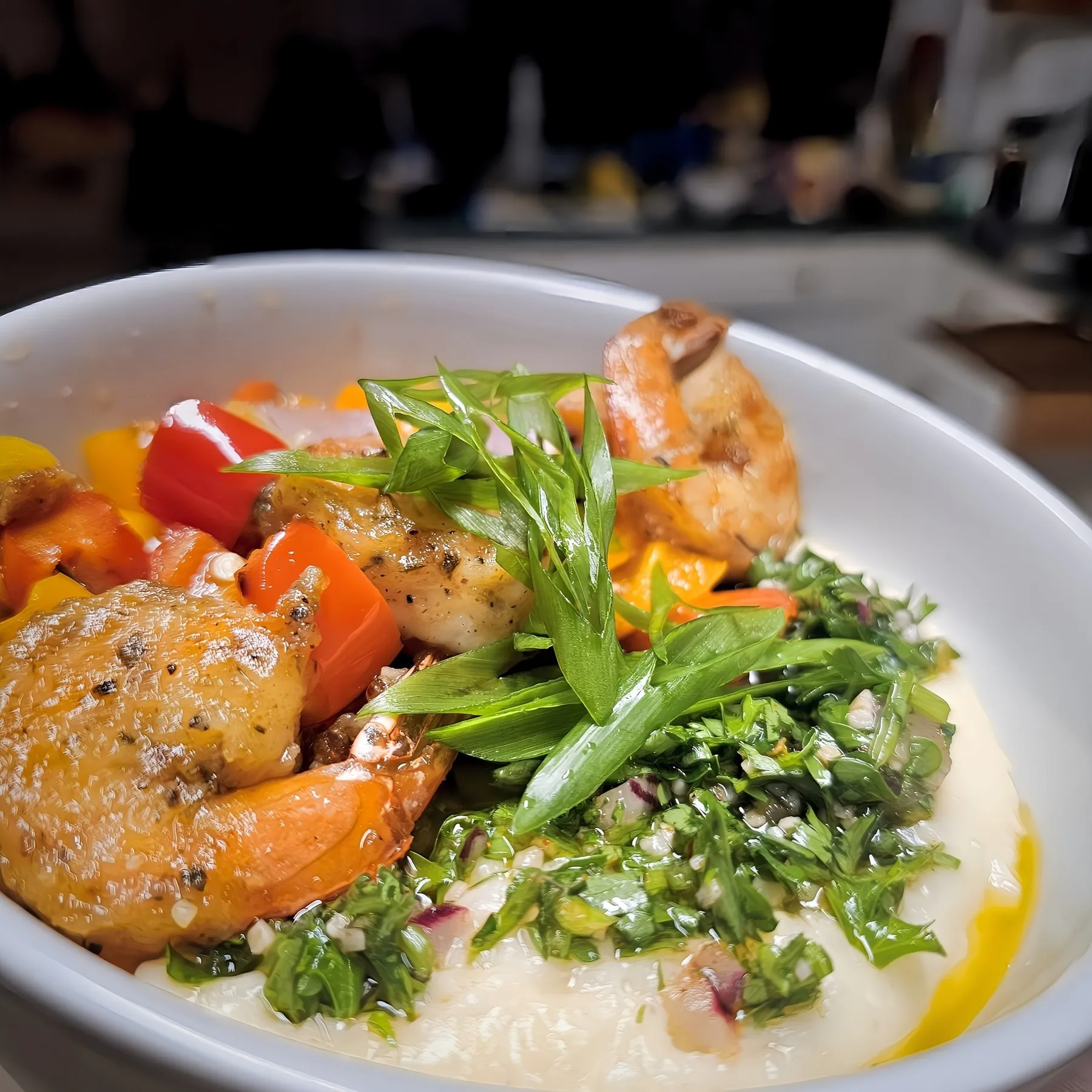 Shrimp, peppers, and scallions over creamy grits, with chimichurri on the side of the white bowl.